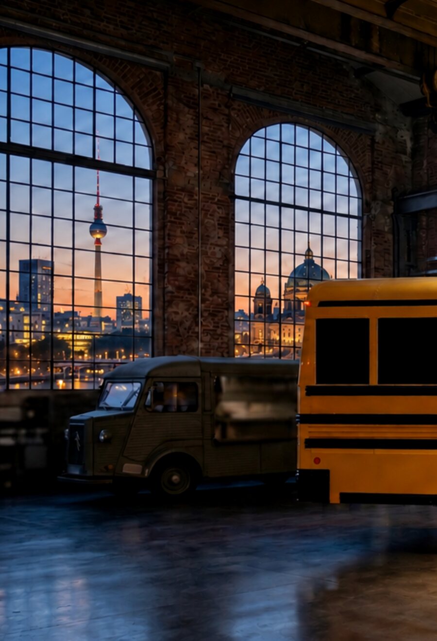 Arched factory windows at dusk with the Berlin television tower on the skyline, a vintage van parked inside the hall.